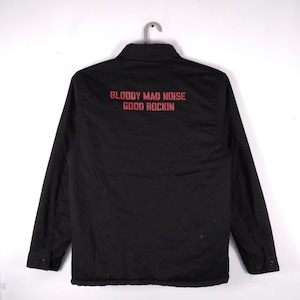 May include: Black long-sleeved shirt with a button-up collar. The back of the shirt has red text that reads "BLOODY MAD NOISE GOOD ROCKIN".