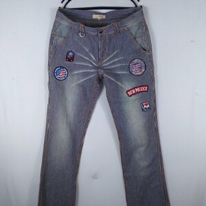 May include: Blue and white striped jeans with multiple embroidered patches, including a red, white, and blue American flag patch, a red and white "New Mexico" patch, and a red, white, and blue "I Love USA" patch.