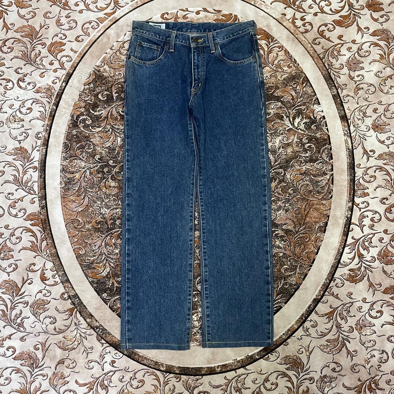Puede incluir: Vaqueros de mezclilla azules con un dise&ntilde;o cl&aacute;sico de cinco bolsillos. Los vaqueros tienen un corte de pierna recta y cierre de bot&oacute;n y cremallera. La mezclilla tiene un lavado medio con detalles sutiles de desvanecimiento y bigotes.