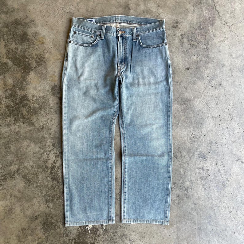 May include: Pale blue denim jeans with a traditional five-pocket design. The jeans have a straight leg cut and a faded wash, giving them a vintage appearance. The jeans are made of durable denim material and feature a button and zip closure.
