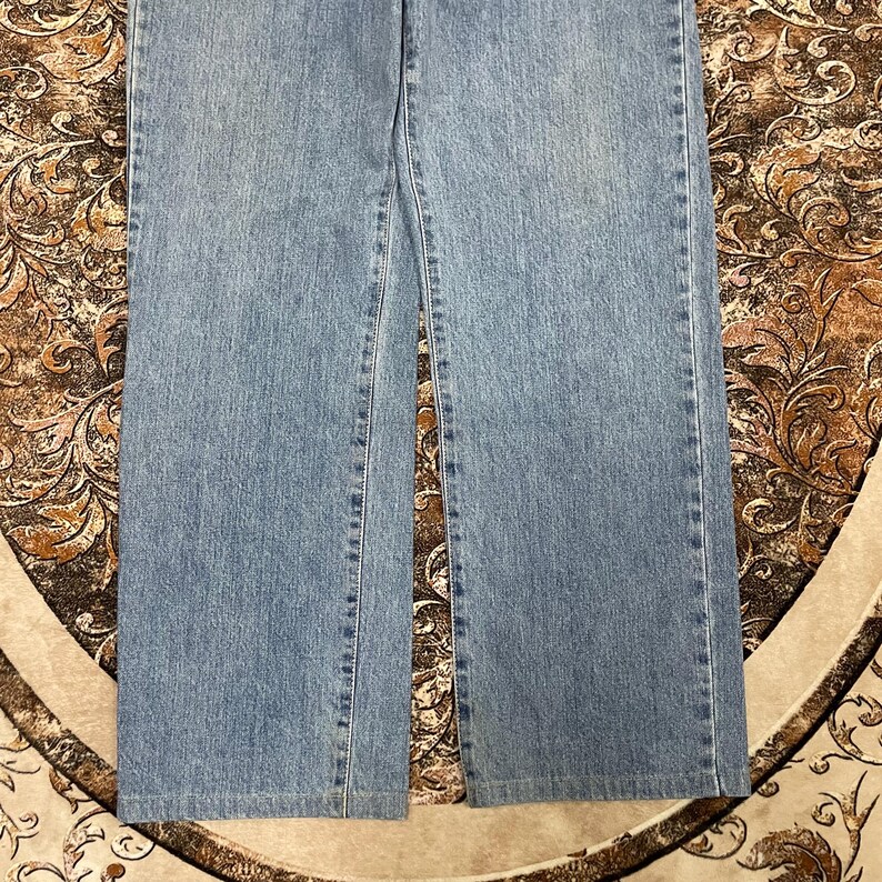 May include: A pair of light blue denim jeans featuring a straight-leg cut with visible vertical stitching along the outer seams and inner legs. The fabric displays a consistent medium-wash texture with classic orange-toned thread detailing.