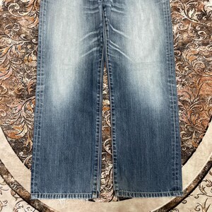 May include: A pair of blue denim jeans featuring a faded wash effect on the thighs and knees. The jeans have a straight-leg cut with visible stitching along the side seams and a classic five-pocket construction with a standard button fly closure.