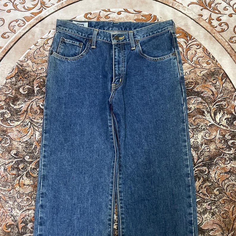 Puede incluir: Vaqueros de mezclilla azul con un dise&ntilde;o cl&aacute;sico de cinco bolsillos. Los vaqueros tienen un corte de pierna recta y un cierre de bot&oacute;n y cremallera. La mezclilla tiene un lavado medio con decoloraci&oacute;n sutil y marcas de desgaste.