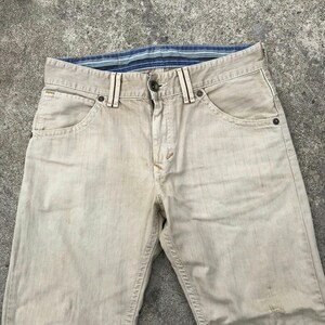 May include: A pair of light beige denim jeans with a blue and white striped waistband.