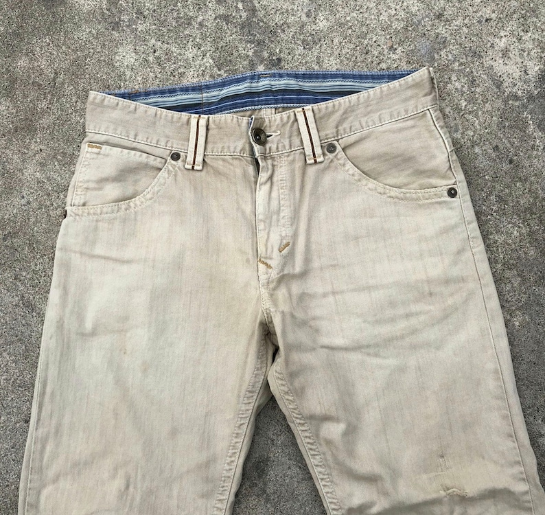 May include: A pair of light beige denim jeans with a blue and white striped waistband.
