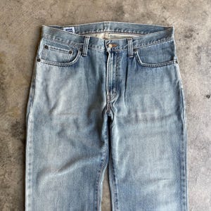 May include: Light blue denim jeans with a classic five-pocket design. The jeans have a faded wash and a straight leg cut. The front features a button closure and a zipper fly. The jeans are made of a durable denim material.