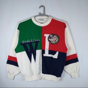 Puede incluir: Una sudadera blanca, roja, verde y azul con una gran "W" y "L" en la parte delantera. La "W" está bordada con el texto "Wike & Sons" y la "L" tiene un pequeño parche bordado de un perro con un sombrero y gafas de sol. El parche dice "The Palm Garden Best Sports".