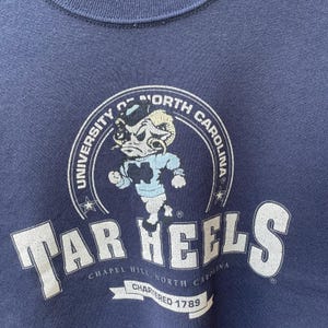 May include: Navy blue sweatshirt featuring the University of North Carolina Tar Heels logo. The logo includes a ram mascot in light blue and white, with the words "Tar Heels" and "University of North Carolina" in white.