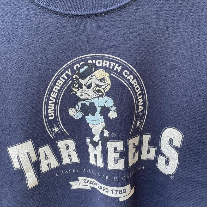 May include: Navy blue sweatshirt featuring the University of North Carolina Tar Heels logo. The logo includes a ram mascot in light blue and white, with the words "Tar Heels" and "University of North Carolina" in white.