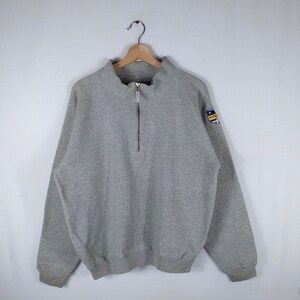 May include: A gray quarter-zip sweatshirt with a small embroidered patch on the right sleeve. The patch features a crest with the word "Royce" in blue.