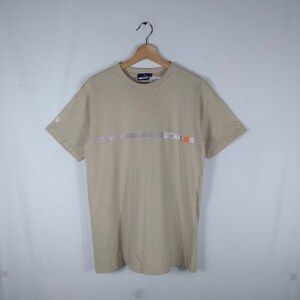 May include: A beige short-sleeved t-shirt with a silver and orange GOTCHA logo on the front.