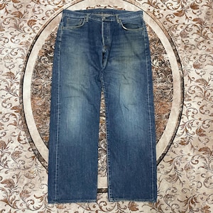 May include: A pair of blue denim jeans featuring a classic five-pocket design, a button fly closure, and a faded wash finish. The jeans have a straight-leg cut with visible whiskering and light distressing on the front thighs and pockets.