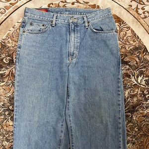 May include: Light blue denim jeans featuring a classic five-pocket design, a metal button closure, a zippered fly, and a small red rectangular label with the text EDWIN stitched onto the interior waistband near the back center.