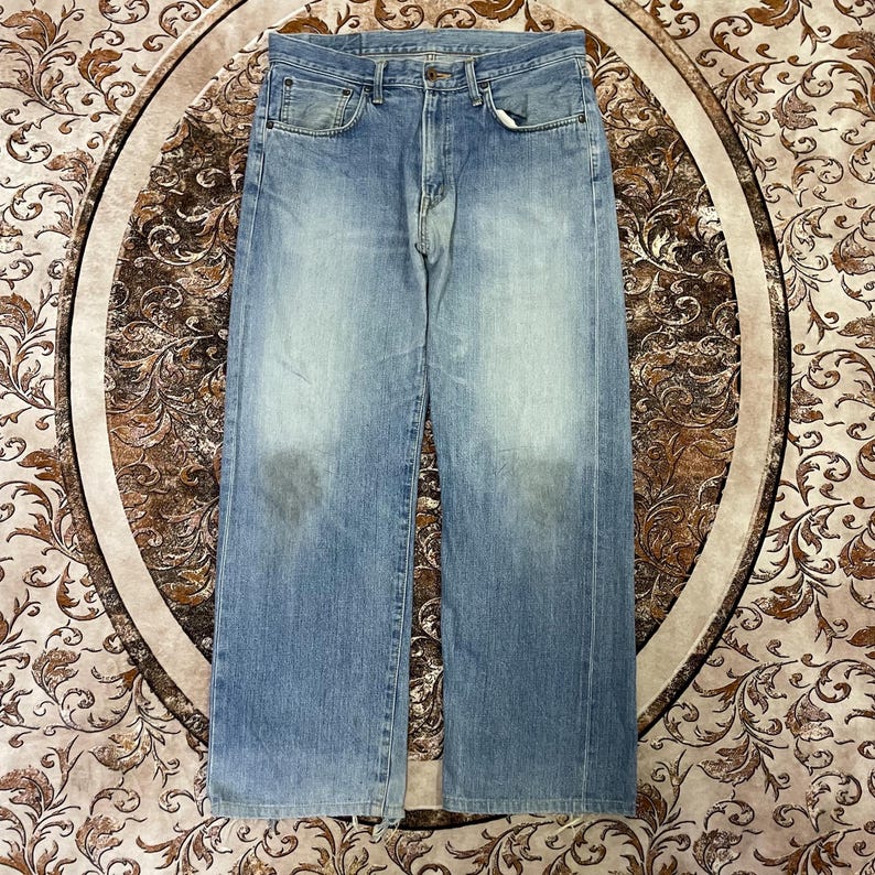 May include: Light blue denim jeans with a classic five-pocket design. The jeans have a faded wash and a straight leg fit. The jeans are made of a durable denim material and feature a button and zipper closure.