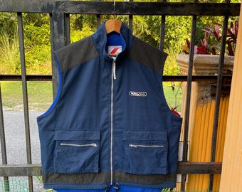 May include: A navy blue Waydo vest with a full-length zip, two front pockets, and a high collar. The vest has brown shoulder and hem detailing. The Waydo logo is on the chest.