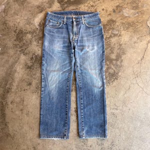 Pu&ograve; includere: Jeans di denim blu sbiadito con un classico design a cinque tasche. I jeans hanno un taglio dritto e mostrano segni di usura, con macchie pi&ugrave; chiare e sottili segni di usura. I jeans sono di lavaggio medio e hanno una chiusura con bottone e cerniera.