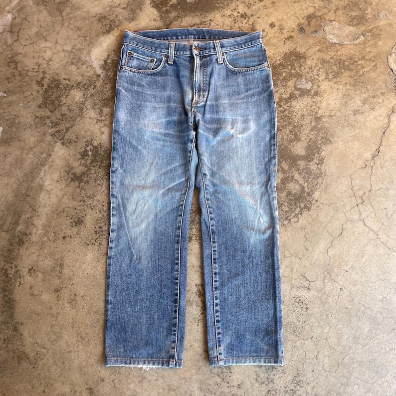 Pu&ograve; includere: Jeans di denim blu sbiadito con un classico design a cinque tasche. I jeans hanno un taglio dritto e mostrano segni di usura, con macchie pi&ugrave; chiare e sottili segni di usura. I jeans sono di lavaggio medio e hanno una chiusura con bottone e cerniera.