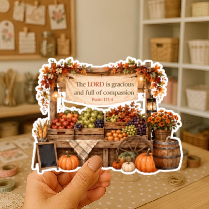 May include: A die-cut sticker featuring a wooden farm stand overflowing with autumn produce, including pumpkins, apples, and grapes. A banner reads, The LORD is gracious and full of compassion, Psalm 111:4. The stand is decorated with fall foliage.