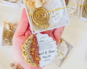 Puede incluir: Cajas de regalo de boda blancas y doradas con un sello de cera y flores secas. Las cajas contienen una pequeña tarjeta con el texto "Ismail & Shams" y la fecha "28.5.23".