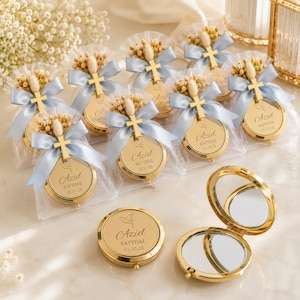 Può includere: Una collezione di specchietti tascabili rotondi in metallo dorato, incisi con il nome Aziel, la parola BAPTISM e la data 10.10.26. Ogni specchietto è decorato con un fiocco in nastro di raso azzurro, una piccola croce dorata e fiori secchi.