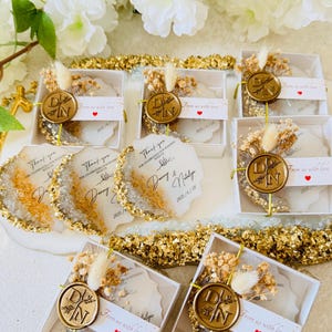 May include: Gold and white wedding favor boxes with a wax seal and dried flowers. The boxes have a thank you message and the date of the wedding. The text reads "Thank you for celebrating our wedding with us. Danny & Natalie 2023/1/28. From us with love."