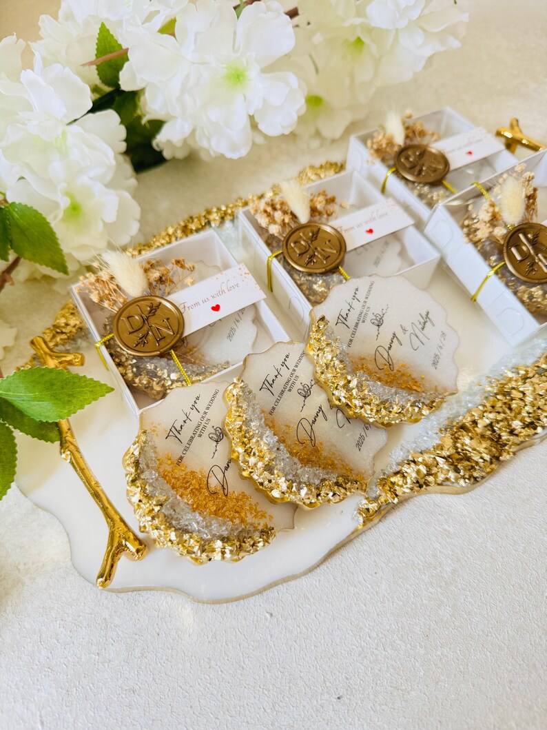 May include: A set of four white and gold resin coasters with a thank you message and the date 2023.11.18. The coasters are displayed on a white tray with a gold branch.