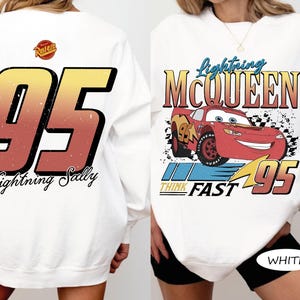 May include: White sweatshirt featuring a graphic of Lightning McQueen from the movie Cars. The front design includes the text "Lightning McQueen" and "Think Fast 95". The back displays a large "95" with "Lightning Sally" below.