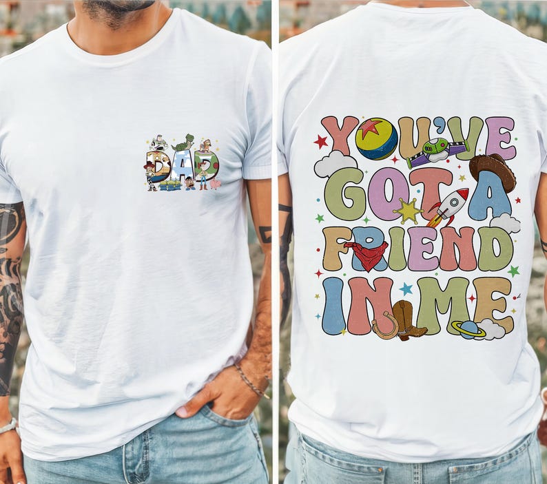 May include: White t-shirt with a colorful graphic design. The front features the word "DAD" with cartoon characters. The back displays the phrase "YOU'VE GOT A FRIEND IN ME" with various illustrations, including a rocket and cowboy boots.