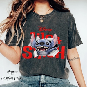 Puede incluir: Camiseta gris oscuro con el personaje de Disney Stitch rompiendo la camiseta, con las palabras "Lilo & Stitch" en rojo. La camiseta tambi&eacute;n tiene las palabras "Pepper Comfort Colors" impresas.
