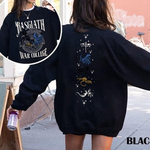 Puede incluir: Sudadera negra con el texto "Basgiath War College" y un dise&ntilde;o de drag&oacute;n en la parte delantera. La parte trasera presenta un dise&ntilde;o vertical de dragones y estrellas. La palabra "BLACK" est&aacute; impresa en la parte inferior derecha.