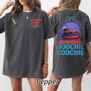 May include: Dark grey t-shirt with the text "WAYDOWN YONDER ON THE Christopher" on the front. The back of the shirt features a graphic of a person in a tube with the text "it gets HOTTER THAN A HOOCHIE COOCHIE".