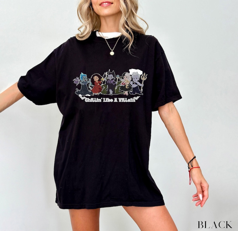 May include: Black t-shirt featuring a graphic of cartoon villains with the text "Chillin' Like A Villain". The shirt has a white collar and is worn by a person. The word "BLACK" is printed at the bottom right.