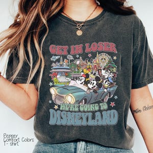Puede incluir: Camiseta gris oscuro con un gr&aacute;fico de Mickey Mouse y sus amigos en un coche antiguo, con el texto "GET IN LOSER WE'RE GOING TO DISNEYLAND". La camiseta es una camiseta Pepper Comfort Colors.
