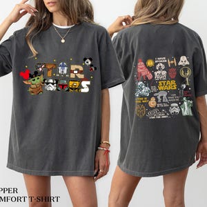 May include: Dark grey Star Wars graphic t-shirt. The front features the words "STAR WARS" with cartoon characters. The back of the shirt has various Star Wars character illustrations and text. The shirt is a comfort t-shirt.