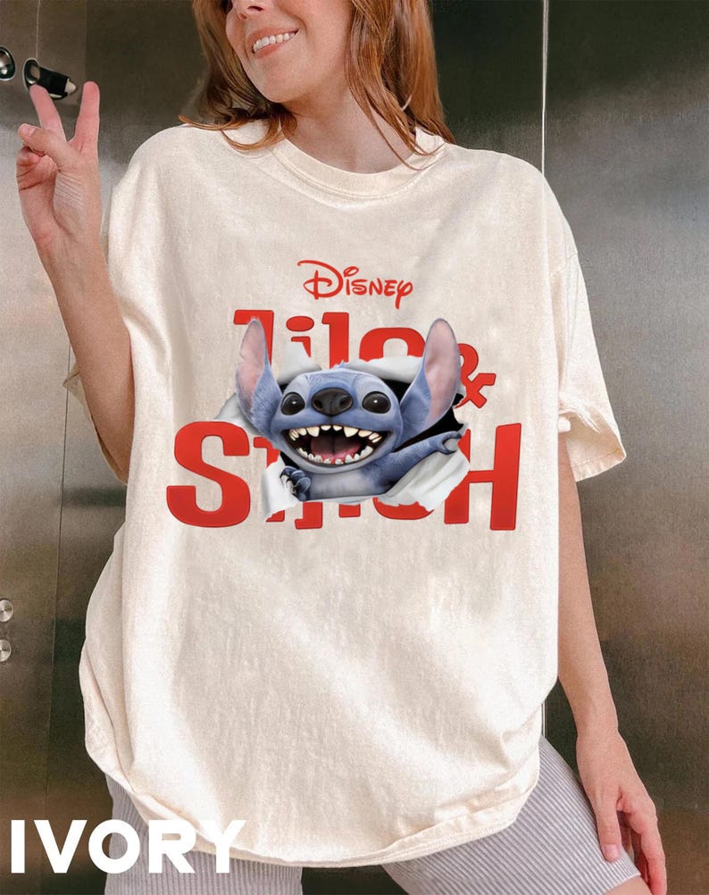 Puede incluir: Camiseta color marfil con el logo de Disney y las palabras "Lilo & Stitch" en rojo. El personaje azul Stitch rompe el texto. La camiseta tiene un corte holgado. La palabra "IVORY" est&aacute; impresa en la parte inferior.