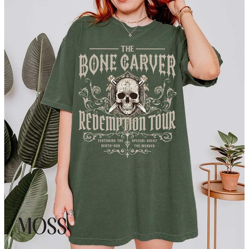 May include: Dark green t-shirt with the text "THE BONE CARVER REDEMPTION TOUR" in a gothic font. The design includes a skull, crossed swords, and decorative flourishes. The shirt also features the text "FEATURING THE DEATH-GOD" and "SPECIAL GUEST THE WEAVER".