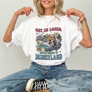 Puede incluir: Camiseta blanca con un dise&ntilde;o gr&aacute;fico retro de Disneyland. El dise&ntilde;o presenta a Mickey Mouse y sus amigos en un coche verde azulado con el texto "Get in Loser, We're Going to Disneyland" en rojo y azul.