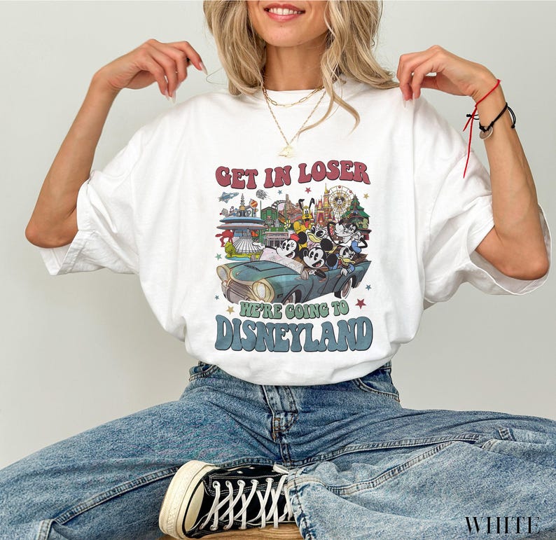 Puede incluir: Camiseta blanca con un dise&ntilde;o gr&aacute;fico retro de Disneyland. El dise&ntilde;o presenta a Mickey Mouse y sus amigos en un coche verde azulado con el texto "Get in Loser, We're Going to Disneyland" en rojo y azul.
