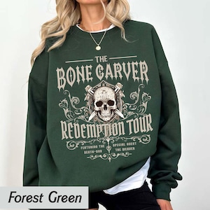 May include: Forest green sweatshirt with a graphic design. The design features the text "THE BONE CARVER REDEMPTION TOUR" with a skull and crossed swords. The sweatshirt is a solid color.