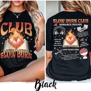 May include: Black t-shirt with a graphic design featuring the text "CLUB SLOW BURN" in orange and white, with a heart-shaped flame over an open book. The back of the shirt has additional text and graphics.