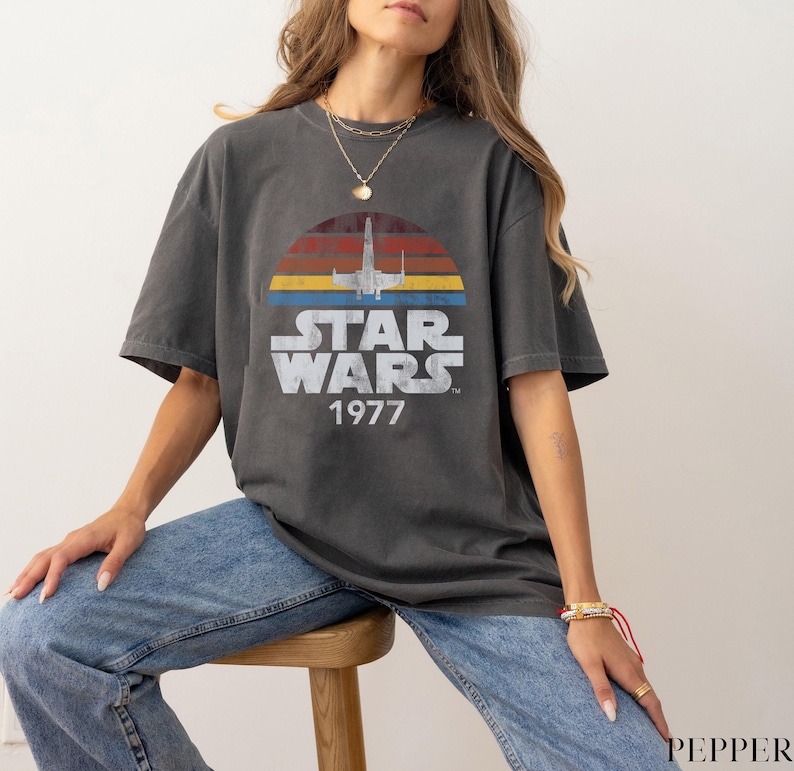 May include: A dark gray t-shirt with a vintage-style Star Wars graphic. The graphic features a spaceship flying through a sunset with the text "Star Wars 1977".