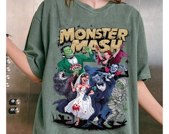 May include: Moss green t-shirt featuring a colorful graphic of classic monsters, including Frankenstein, a werewolf, a vampire, and a mummy. The text "MONSTER MASH" is displayed above the characters. The word "Moss" is printed at the bottom.
