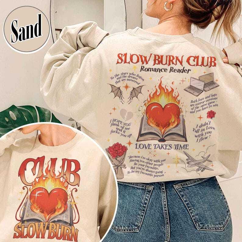 May include: Sand-colored sweatshirt with the text "SLOW BURN CLUB Romance Reader" in red and orange. The design includes a heart on fire, an open book, and various romantic-themed illustrations. The sweatshirt also has the text "LOVE TAKES TIME".