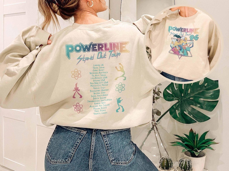K&ouml;nnte beinhalten: Cremefarbenes Sweatshirt mit einem Powerline Stand Out Tour-Aufdruck auf dem R&uuml;cken und einem kleineren Powerline '96-Aufdruck auf der Vorderseite. Das Design zeigt farbenfrohe Schrift und Illustrationen, die eine Retro-Konzert-Atmosph&auml;re erzeugen.