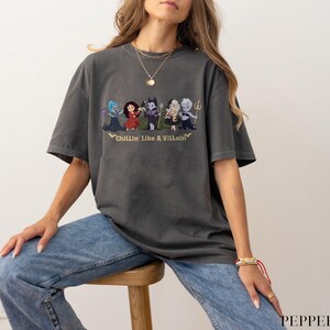 May include: Dark gray t-shirt featuring a graphic of cartoon villains with the text "Chillin' Like A Villain" in gold. The shirt is a relaxed fit and has short sleeves.