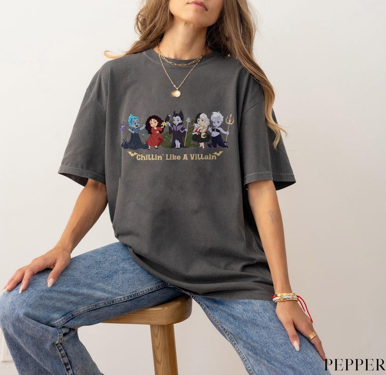 May include: Dark gray t-shirt featuring a graphic of cartoon villains with the text "Chillin' Like A Villain" in gold. The shirt is a relaxed fit and has short sleeves.