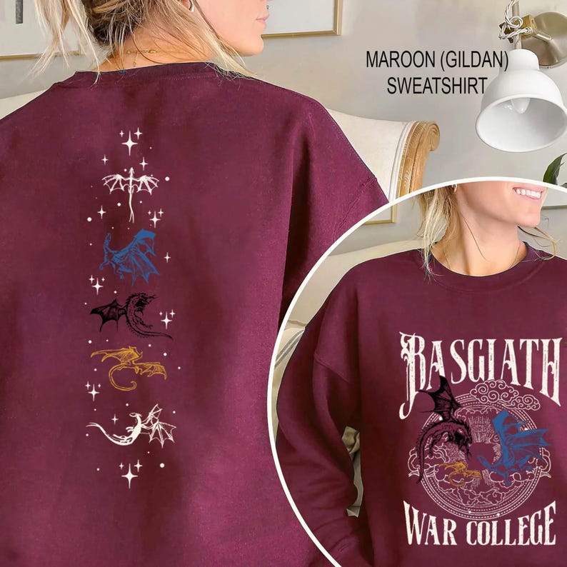 Puede incluir: Sudadera granate con dise&ntilde;o de drag&oacute;n. La parte delantera presenta el texto "BASGIATH WAR COLLEGE" con un gr&aacute;fico de drag&oacute;n. La parte trasera tiene una disposici&oacute;n vertical de ilustraciones de dragones en blanco, azul, negro, dorado y blanco.