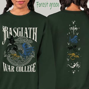Puede incluir: Sudadera verde bosque con texto "Basgiath War College" y gr&aacute;ficos de dragones. La parte delantera presenta un dise&ntilde;o circular con dragones negros, azules y amarillos. La parte trasera muestra una l&iacute;nea vertical de ilustraciones de dragones en blanco, azul, negro, dorado y blanco.