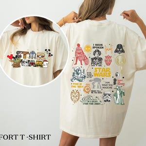 May include: Sand-coloured comfort t-shirt with Star Wars characters and logos. The front shows a Star Wars logo with Baby Yoda and Mickey Mouse ears. The back has various Star Wars graphics and text, including "I Have Spoken" and "This is the Way."