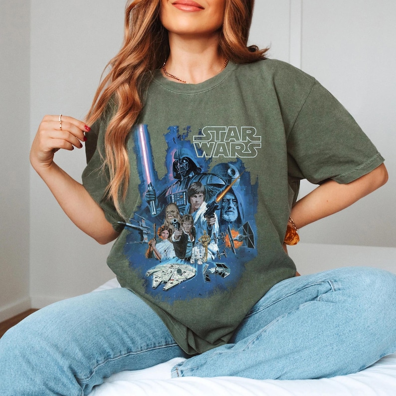 May include: A green t-shirt with a vintage-style Star Wars graphic featuring Darth Vader, Luke Skywalker, Han Solo, Princess Leia, and other characters. The text "STAR WARS" is printed in white above the graphic.